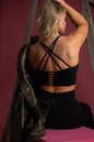 Alyth Active women's black sports crop bra featuring a crisscross strappy open back and horizontal cutout details, modeled with black leggings.