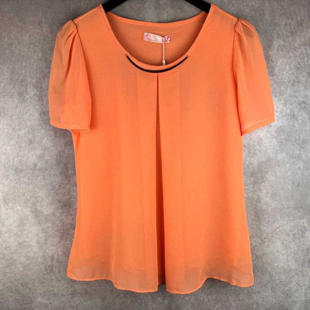 An orange short-sleeve blouse with a scoop neckline and a thin black curved trim detail, hanging on a black hanger against a textured gray background.