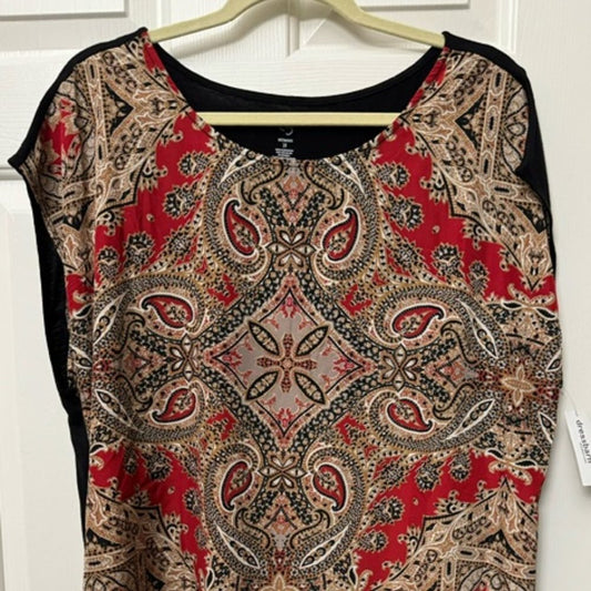 A women's short-sleeve top with a vibrant red, beige, and black paisley pattern, hanging on a wooden hanger against a white paneled door.