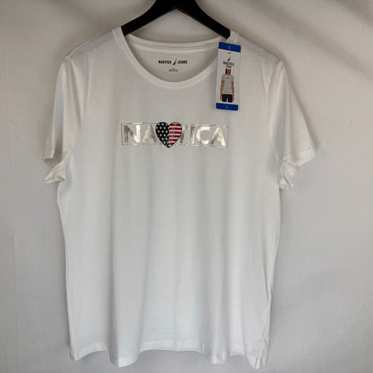 A white short-sleeve crewneck t-shirt by Nautica, hanging on a black hanger against a light gray wall. The front features a graphic spelling 'NAUTICA' with a heart made of an American flag pattern (red, white, and blue).