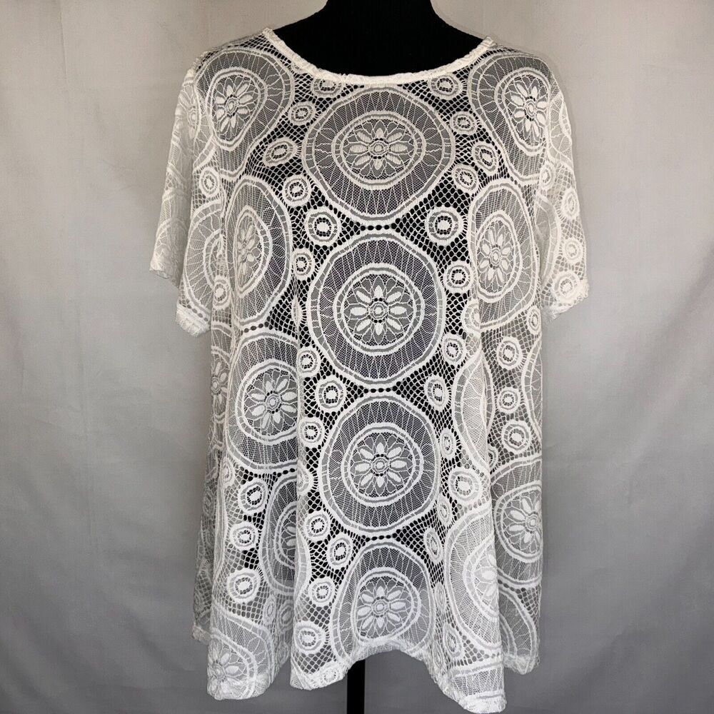 White lace short-sleeve top with circular floral mandala patterns, displayed on a black mannequin torso against a light gray fabric backdrop.