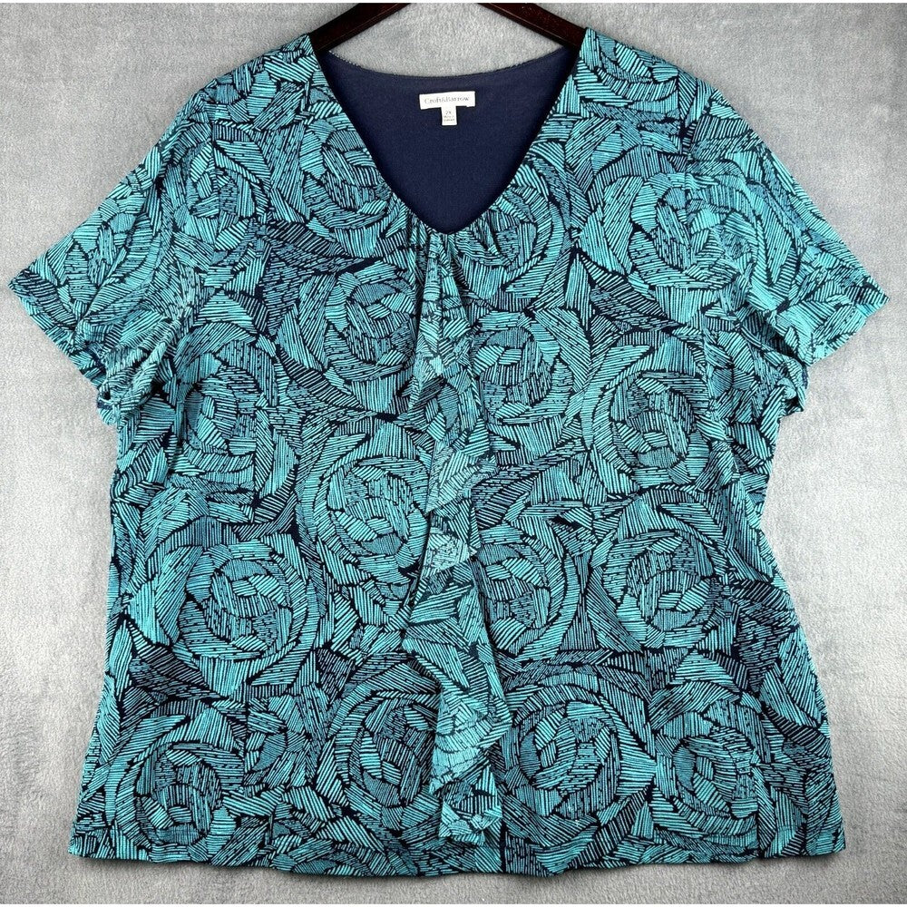 A short-sleeve V-neck blouse with a teal and navy blue abstract floral pattern, hanging on a dark hanger against a gray textured background.