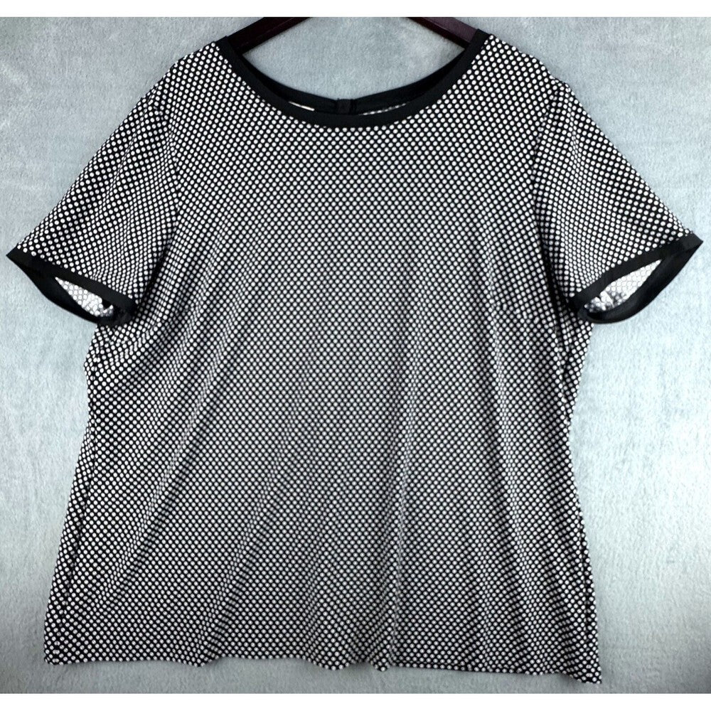 A black and white micro-dot patterned short-sleeve t-shirt with solid black trim on the crew neck and sleeve cuffs, displayed flat on a hanger against a light gray textured background.