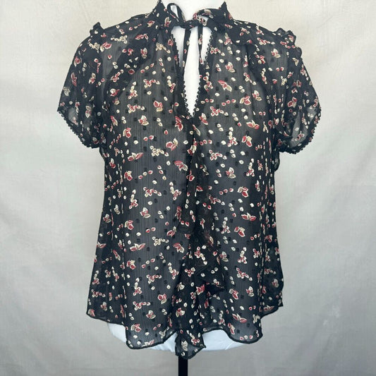 A sheer black short-sleeve blouse with a red and white floral print, featuring a tie-neck detail and ruffled trim, displayed on a mannequin torso against a light gray fabric backdrop.