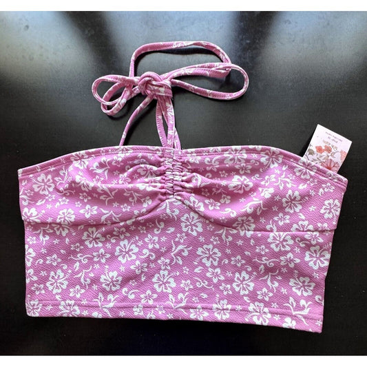 A pink and white floral print halter bikini top with a ruched center front, laid flat on a dark surface with a brand tag attached.