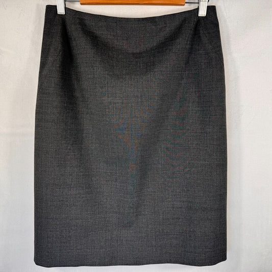 A dark charcoal gray textured pencil skirt hanging from a wooden hanger with white clips against a white fabric backdrop.