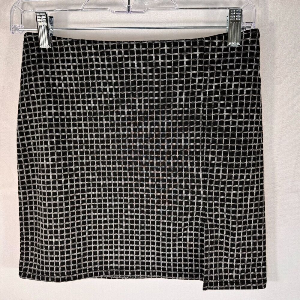 A black and white grid-patterned skirt hanging from a clear plastic hanger with silver clips against a white wall.