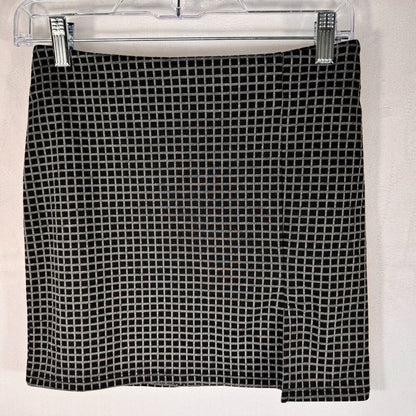 A black and white grid-patterned skirt hanging from a clear plastic hanger with silver clips against a white wall.