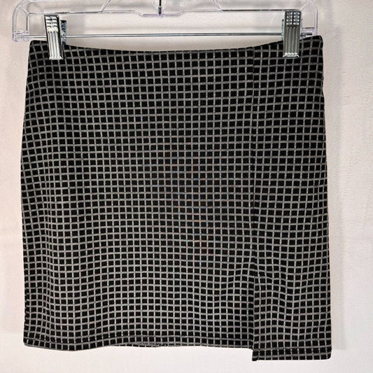 A black and white grid-patterned skirt hanging from a clear plastic hanger with silver clips against a white wall.