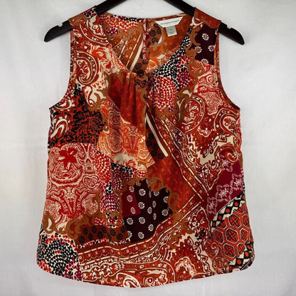 A sleeveless wrap-style blouse with a ruffled tie neckline, featuring a busy patchwork paisley and floral print in red, orange, brown, black, and cream, hanging on a black hanger against a white background.