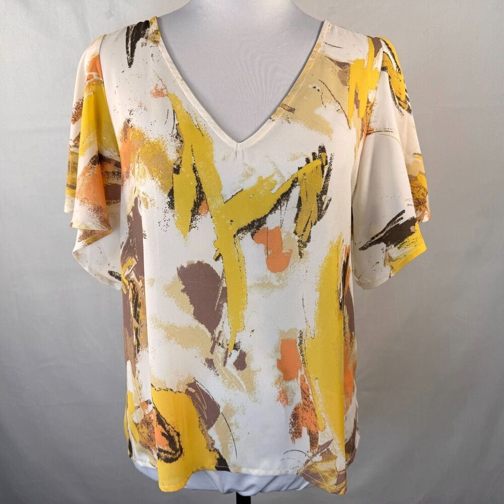 A short-sleeve V-neck blouse with an abstract painterly print in yellow, orange, brown, and beige on a white base, displayed on a mannequin torso against a light gray backdrop.