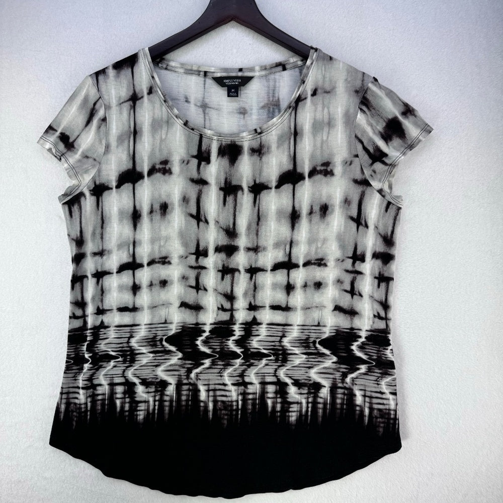 A short-sleeve scoop-neck top with a black and white tie-dye pattern and a black gradient hem, hanging on a black hanger against a white wall.