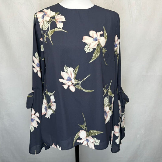 A navy blue long-sleeve blouse with a white and pink floral print, displayed on a mannequin against a light gray fabric backdrop.