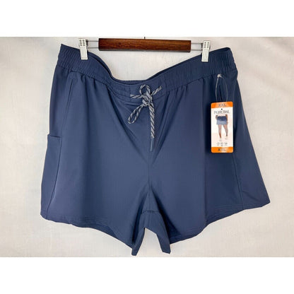 A pair of women's navy blue athletic shorts with a gray and white striped drawstring, hanging on a wooden hanger with white clips against a light beige fabric backdrop. A retail hangtag is attached to the side.