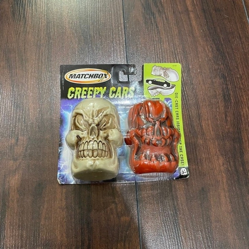 Matchbox Creepy Cars oil change cap set featuring a beige skull cap and a red monster head cap, in original blister packaging on a dark wood background.