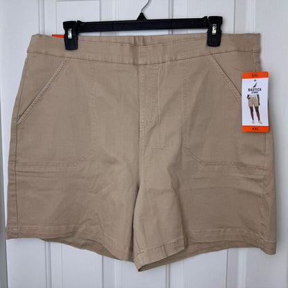 A pair of women's khaki shorts hanging on a black hanger against a white paneled door. The shorts have a flat front, side pockets, and a hangtag on the right side that reads 'NORTHERN' and 'XXL'.