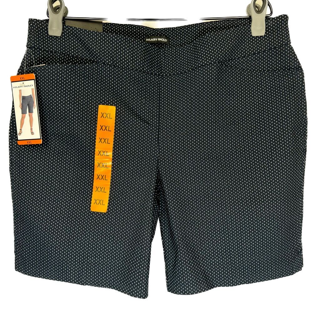 A pair of women's black shorts with a small white polka dot pattern, hanging from silver metal clips. The shorts still have their retail tags attached, including a yellow size tag indicating XXL and a brand tag that reads 'SILK CITY PARIS'.