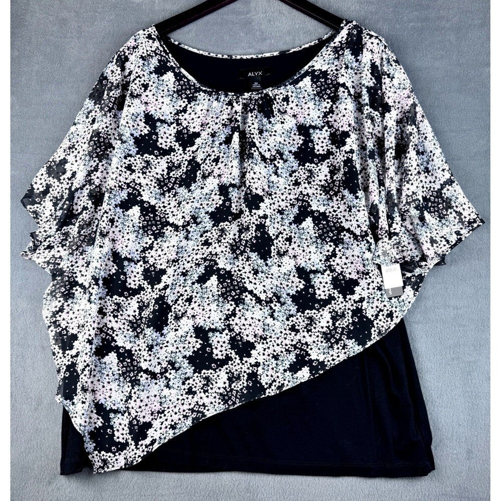 A women's short-sleeve top with a black and white floral print, layered over a solid black undergarment or skirt, displayed on a black hanger against a gray textured background.