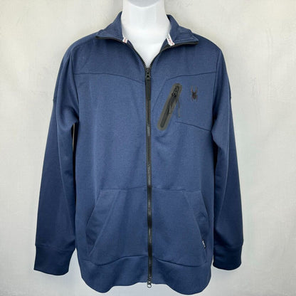 A navy blue zip-up jacket with a stand collar, displayed on a white mannequin torso against a light gray textured wall. The jacket features a vertical zippered pocket on the left chest with a small embroidered spider logo, and a small silver zipper pull on the right pocket.