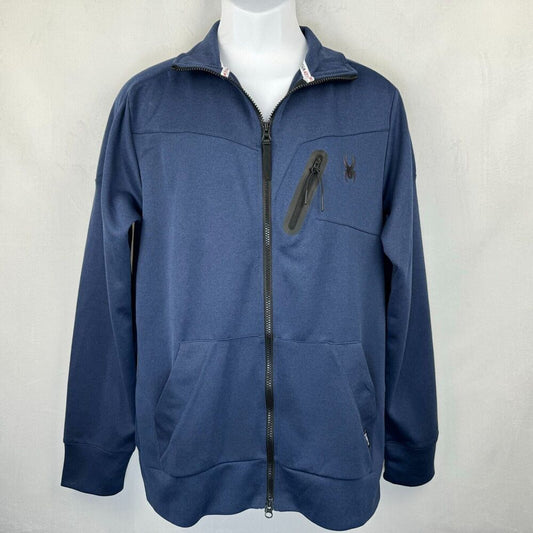 A navy blue zip-up jacket with a stand collar, displayed on a white mannequin torso against a light gray textured wall. The jacket features a vertical zippered pocket on the left chest with a small embroidered spider logo, and a small silver zipper pull on the right pocket.