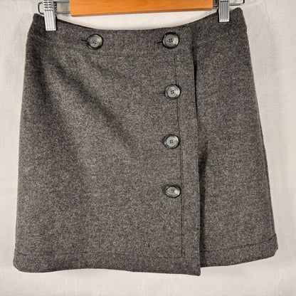 A gray textured wool skirt with a button-front wrap design, hanging on a wooden hanger against a light fabric backdrop.