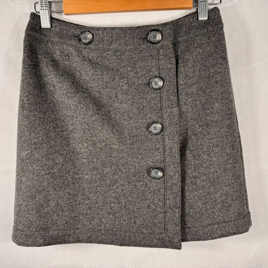 A gray textured wool skirt with a button-front wrap design, hanging on a wooden hanger against a light fabric backdrop.