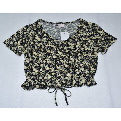 A short-sleeve crop top with a black and beige floral pattern, featuring a V-neckline, front tie detail, and a white price tag attached.