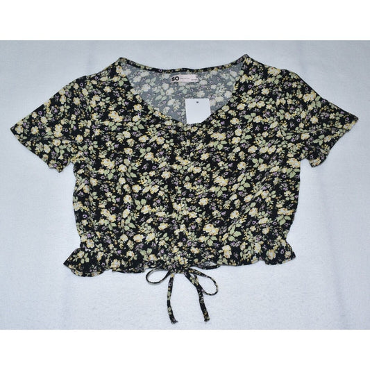 A short-sleeve crop top with a black and beige floral pattern, featuring a V-neckline, front tie detail, and a white price tag attached.