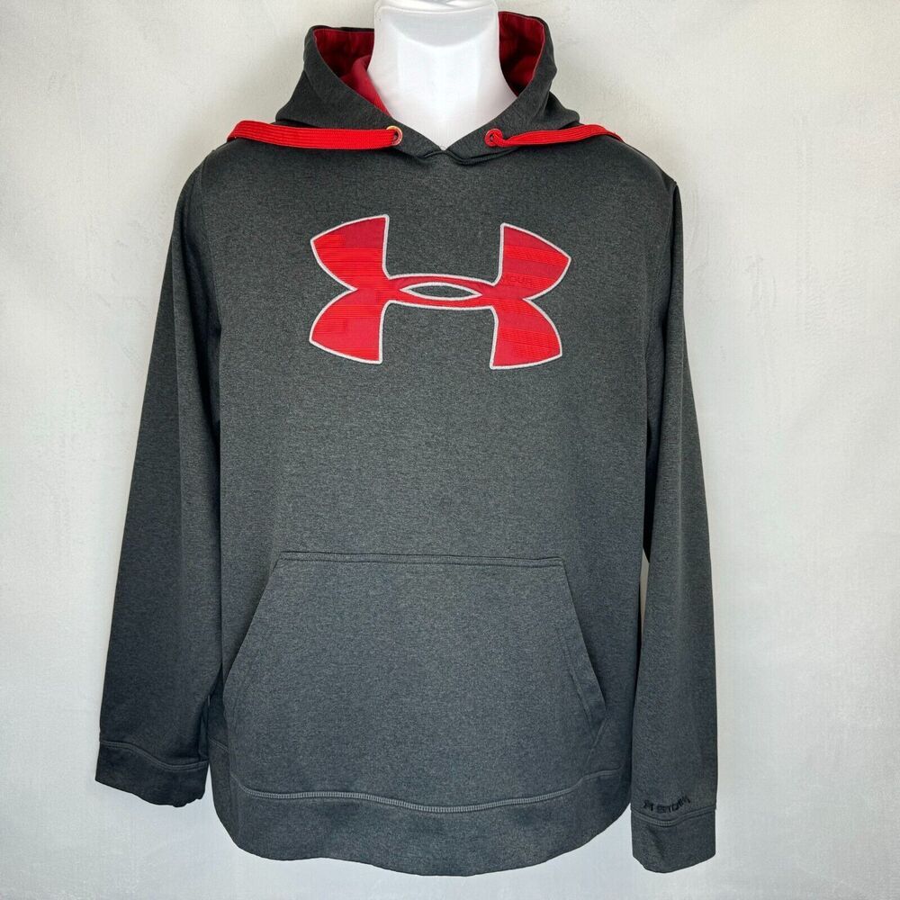 A dark gray Under Armour pullover hoodie with a red Under Armour logo on the chest, a red-lined hood, and a front kangaroo pocket, displayed on a white mannequin torso against a light gray background.