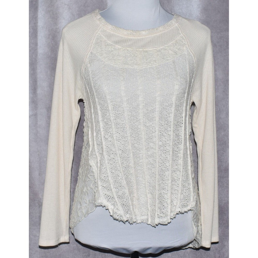 An off-white long-sleeve knit top with a textured lace-like front panel and ribbed sleeves, displayed on a mannequin torso against a gray backdrop.