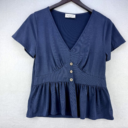 A navy blue short-sleeve V-neck top with a peplum hem and three decorative buttons down the front, hanging on a dark wooden hanger against a light gray textured background.