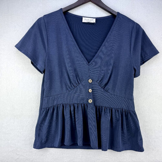 A navy blue short-sleeve V-neck top with a peplum hem and three decorative buttons down the front, hanging on a dark wooden hanger against a light gray textured background.