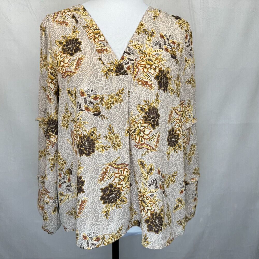 A women's long-sleeve blouse with a V-neckline, displayed on a white mannequin torso. The blouse features an all-over abstract floral pattern in brown, gold, and beige tones on a light cream background.