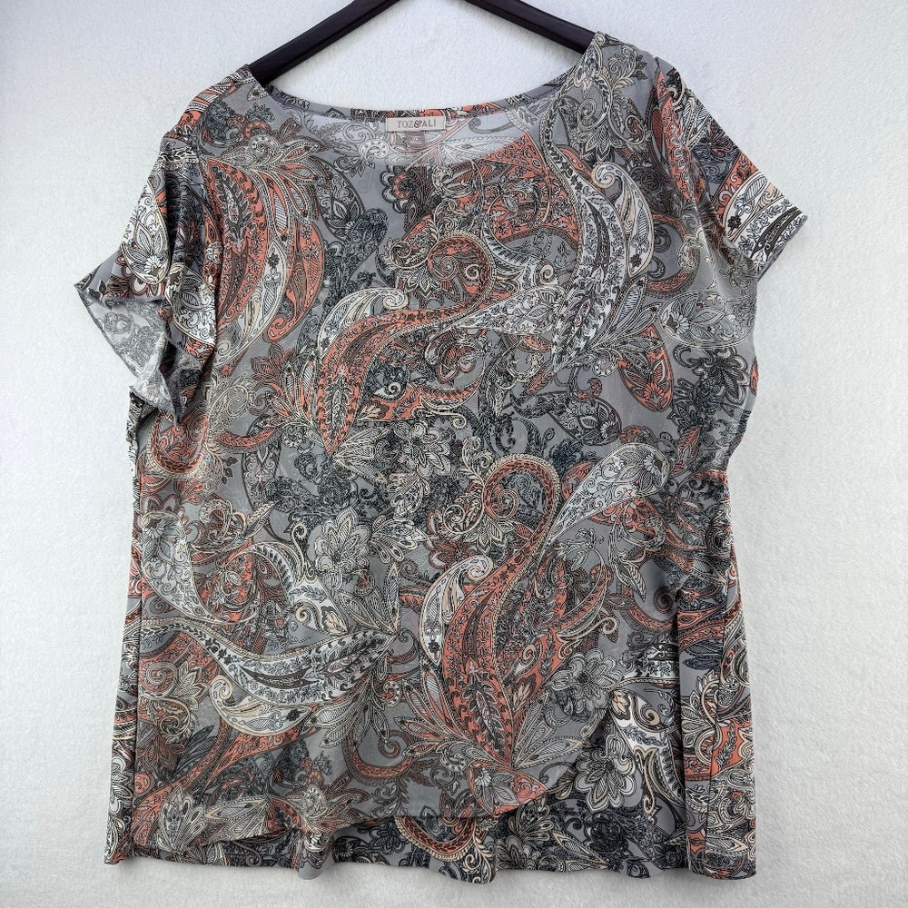 A short-sleeve blouse with a gray, black, and rust-orange paisley pattern, hanging on a black hanger against a light gray textured wall.