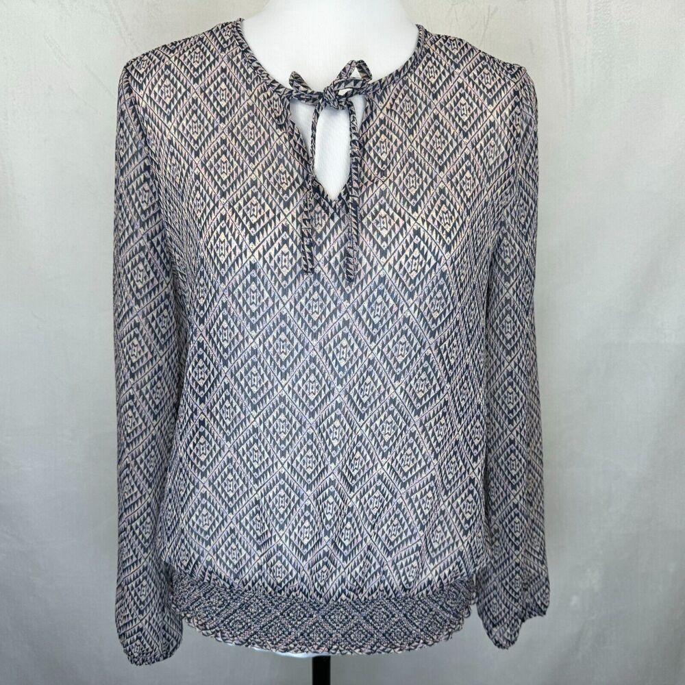 A long-sleeve knit blouse with a blue and white geometric diamond pattern, featuring a keyhole neckline with a tie-front closure, displayed on a white mannequin torso against a light gray fabric backdrop.