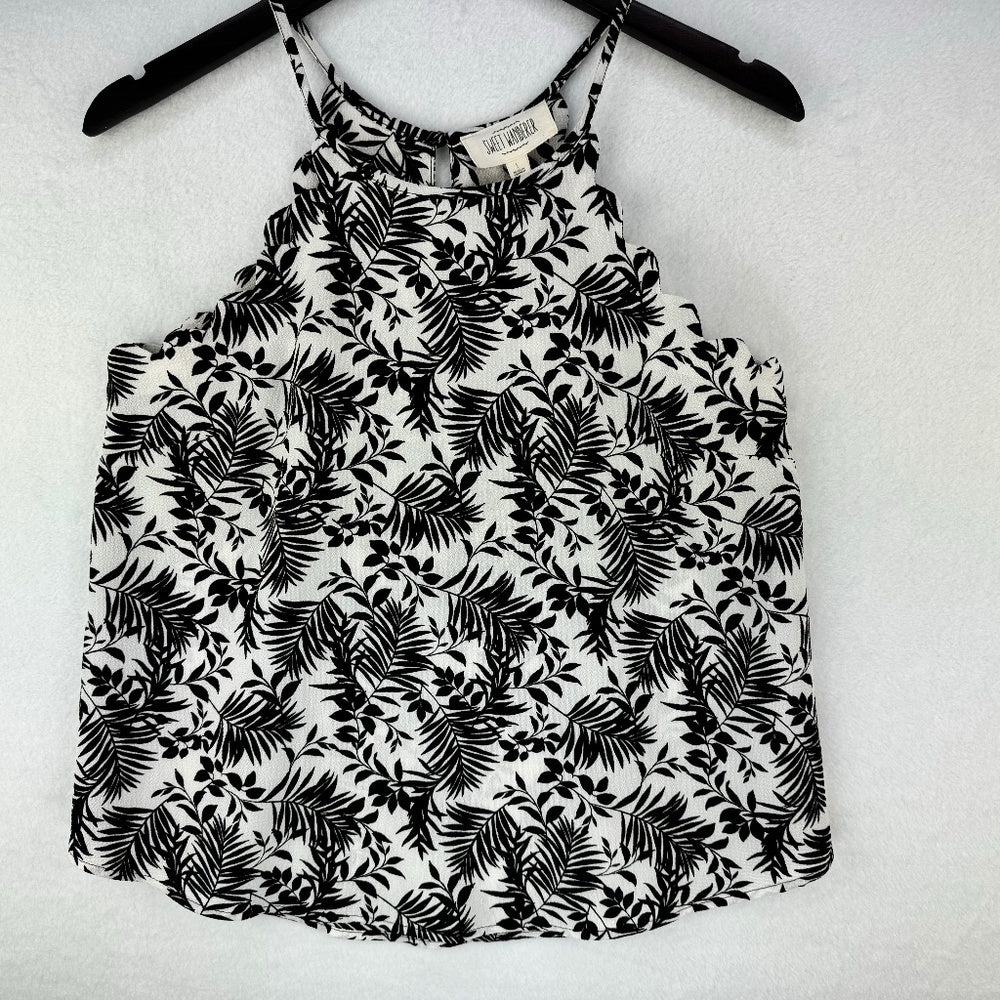 A black and white tropical palm leaf print sleeveless camisole top hanging on a black hanger against a white textured background.