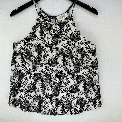 A black and white tropical palm leaf print sleeveless camisole top hanging on a black hanger against a white textured background.