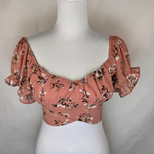 A dusty rose puff-sleeve crop top with a floral print, displayed on a white mannequin torso against a neutral light gray background.