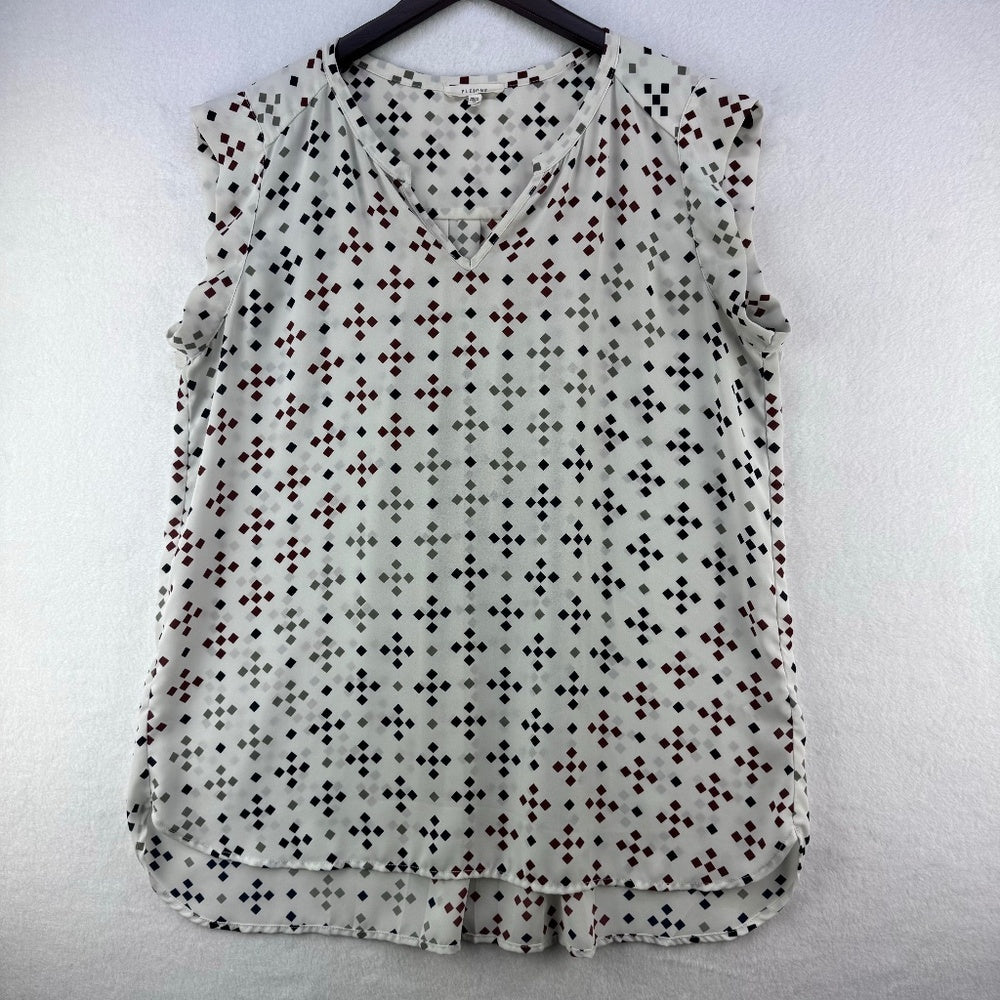 A sleeveless V-neck blouse with a small repeating geometric dot pattern in black, brown, and gray on a light gray base, hanging on a black hanger against a white textured wall.