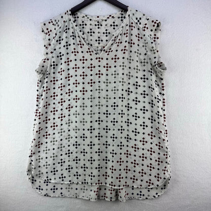 A sleeveless V-neck blouse with a small repeating geometric dot pattern in black, brown, and gray on a light gray base, hanging on a black hanger against a white textured wall.