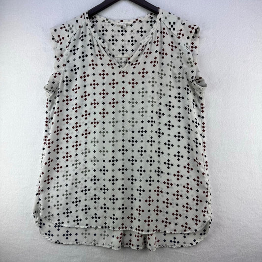 A sleeveless V-neck blouse with a small repeating geometric dot pattern in black, brown, and gray on a light gray base, hanging on a black hanger against a white textured wall.