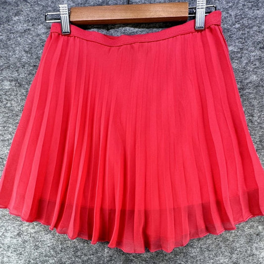 A bright red pleated mini skirt hanging from a wooden hanger with metal clips against a textured gray background.