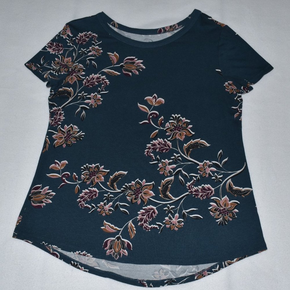 A short-sleeve crewneck top in dark navy blue, featuring a floral vine pattern in muted pink, brown, and beige tones, laid flat on a light gray background.
