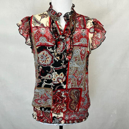 A short-sleeve ruffled blouse with a patchwork paisley print in red, black, beige, and gray, displayed on a mannequin against a light gray backdrop.