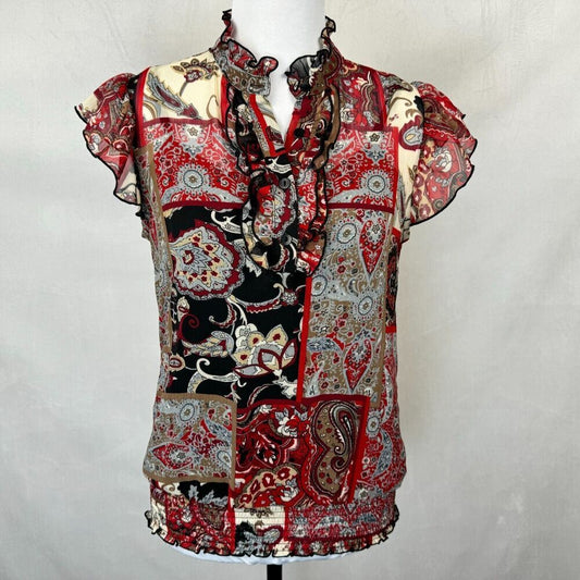 A short-sleeve ruffled blouse with a patchwork paisley print in red, black, beige, and gray, displayed on a mannequin against a light gray backdrop.