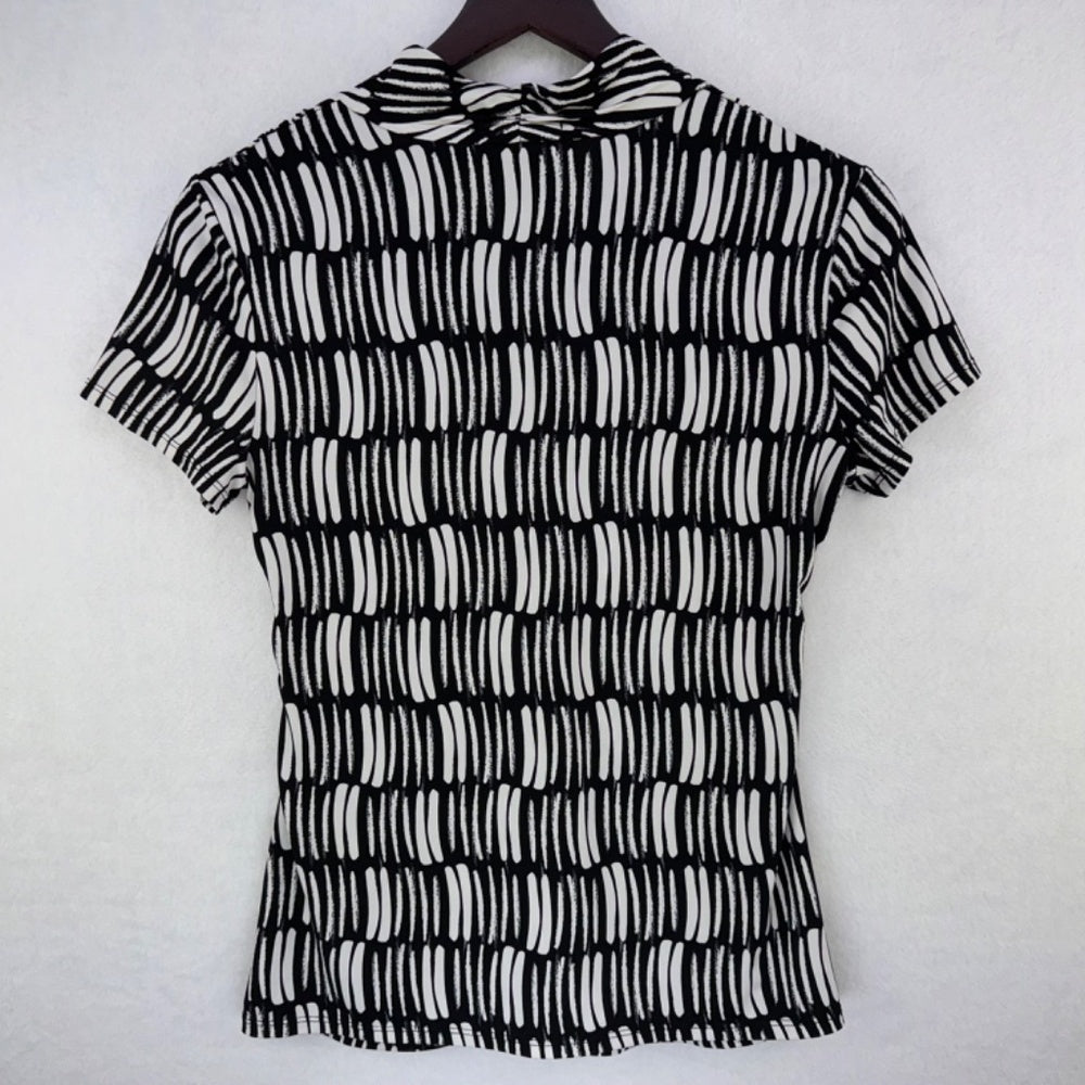 A short-sleeve collared blouse with a black and white abstract wavy stripe pattern, hanging on a dark wooden hanger against a light gray textured wall.