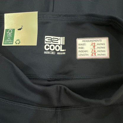 Close-up of the inside neck area of a black athletic top, showing the 32° COOL brand label, a gold care tag, and a white measurement label with waist, rise, inseam, and length measurements.