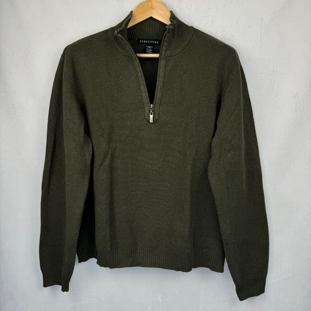 An olive green quarter-zip knit sweater hanging on a wooden hanger against a light gray textured wall.