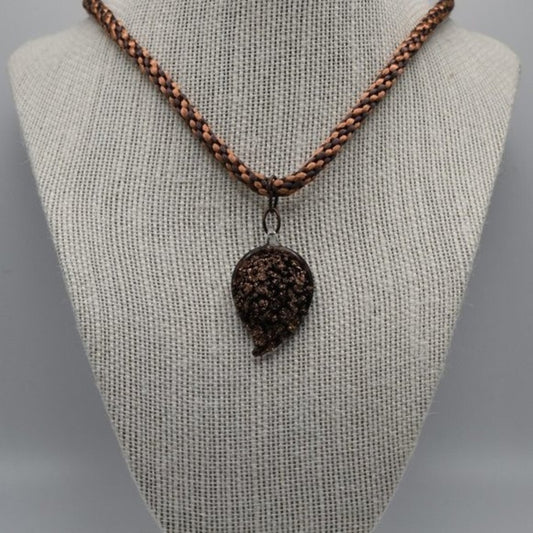 A braided brown cord necklace with a dark brown textured pendant, displayed on a beige fabric-covered jewelry bust against a light gray background.