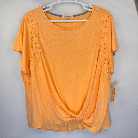An orange short-sleeve knit top with lace trim on the sides, hanging on a white hanger against a light gray wall. A brand tag is visible on the right side.